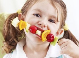 Nena comiendo un brochete de frutas
